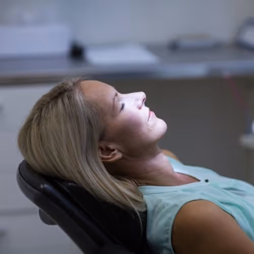 Woman with closed eyes reclining in a dental chair, appearing calm and relaxed.