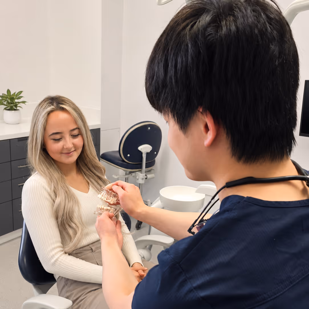 Dentist showing dental models to a female patient sitting in a clinic chair.