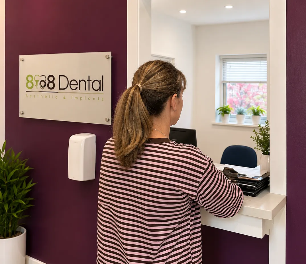 Woman at dental office reception desk with 8f08 Dental sign on purple wall.