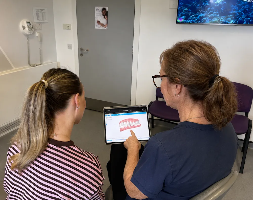 Dentist showing a dental teeth model on a tablet to a patient in a clinic.