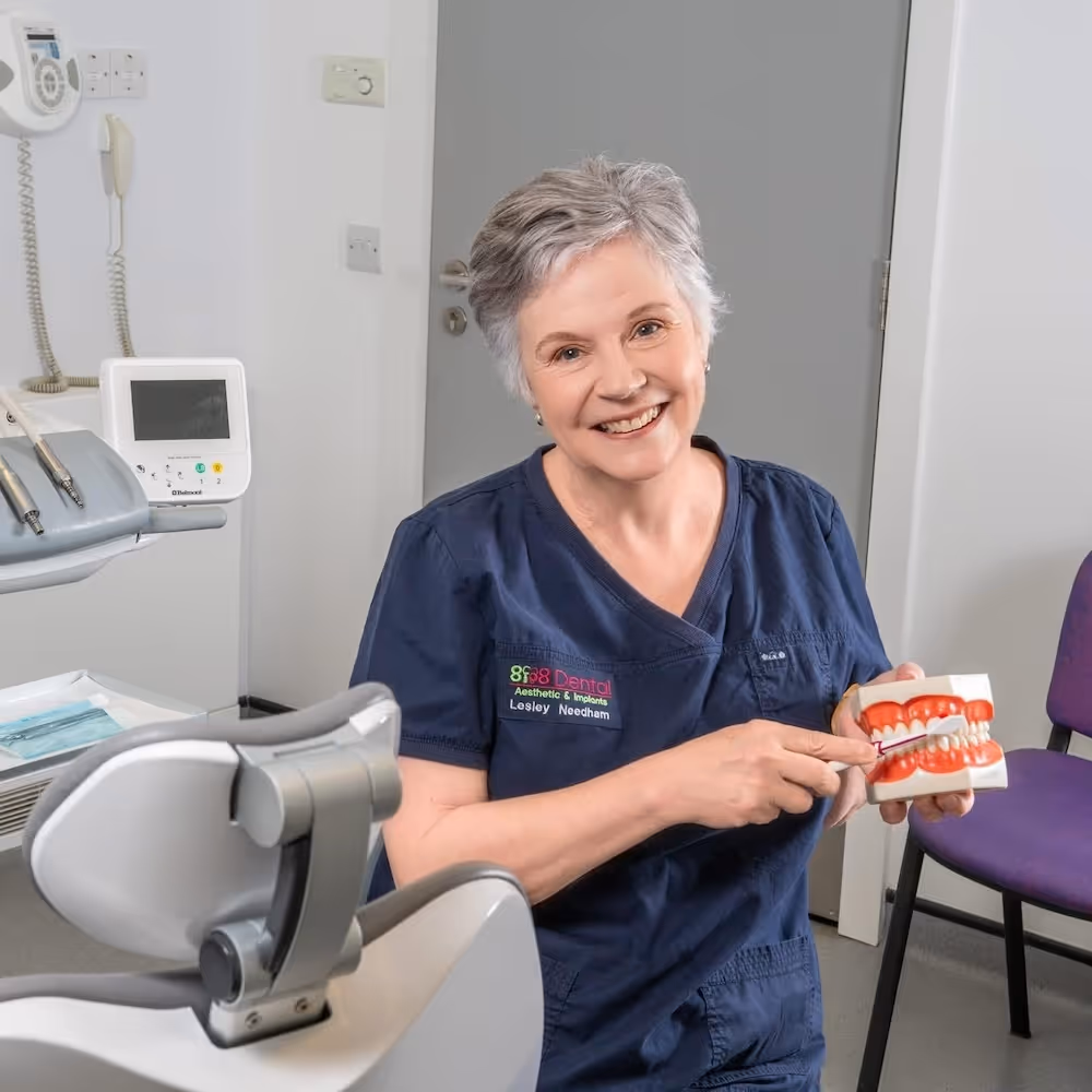 Smiling dental professional in navy scrubs holding a dental model and pointing at the teeth.