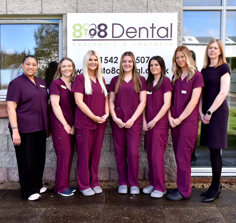 Seven dental staff in purple uniforms standing in front of 8 to 8 Dental clinic sign.