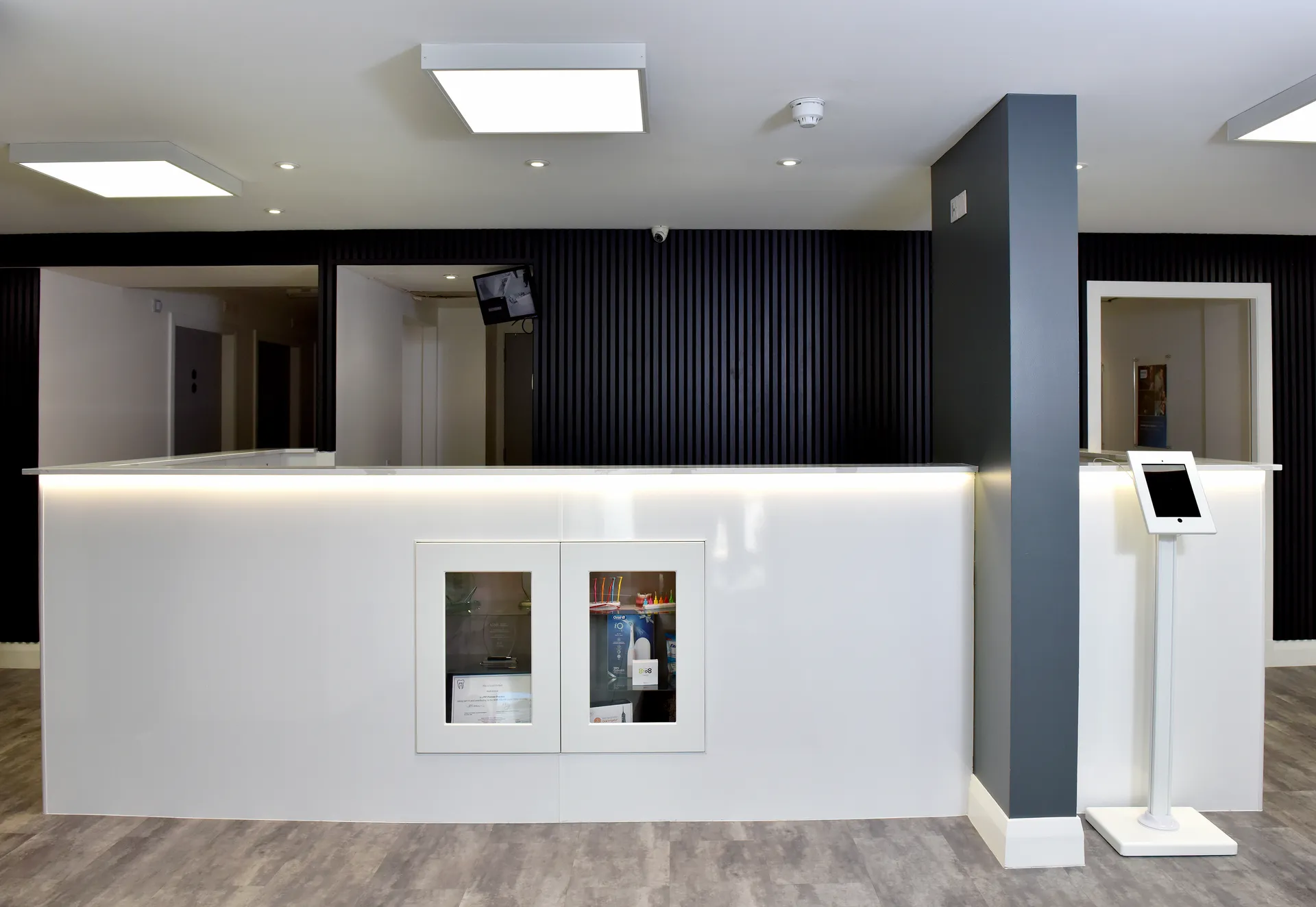 Modern reception desk with illuminated white surface, black wall panels, and a tablet on a stand.