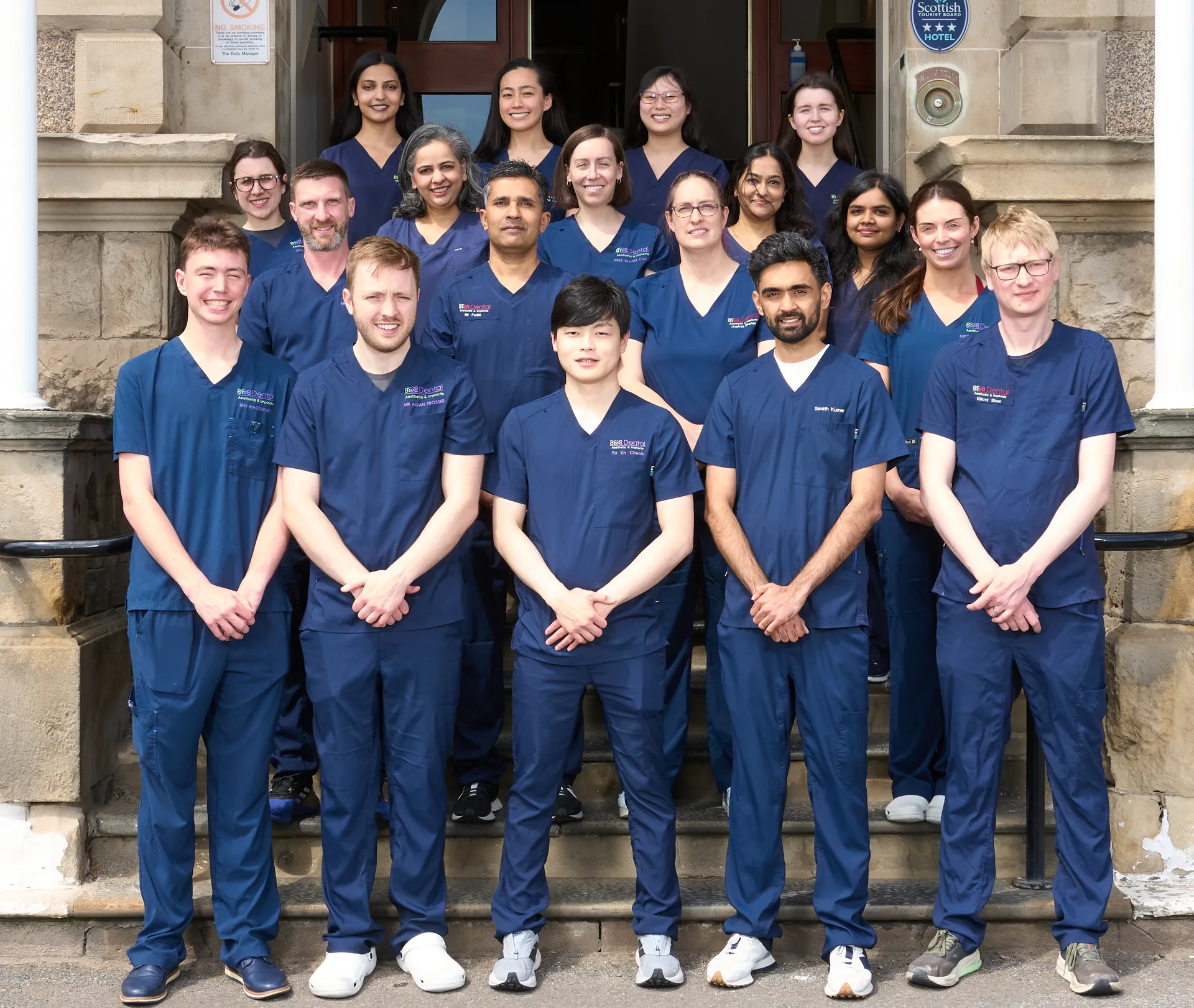 A diverse group of dental professionals in navy scrubs posing on stone steps outside a building.