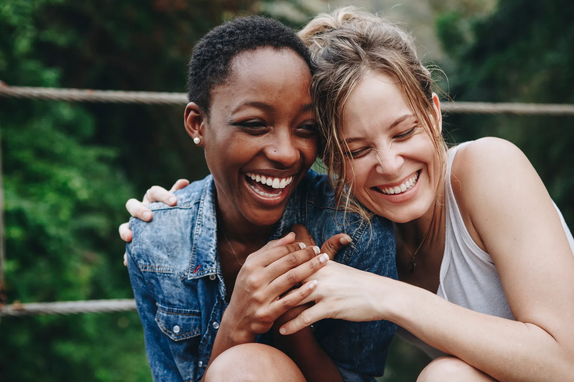 Two women laughing closely together, sharing a joyful and affectionate moment outdoors.