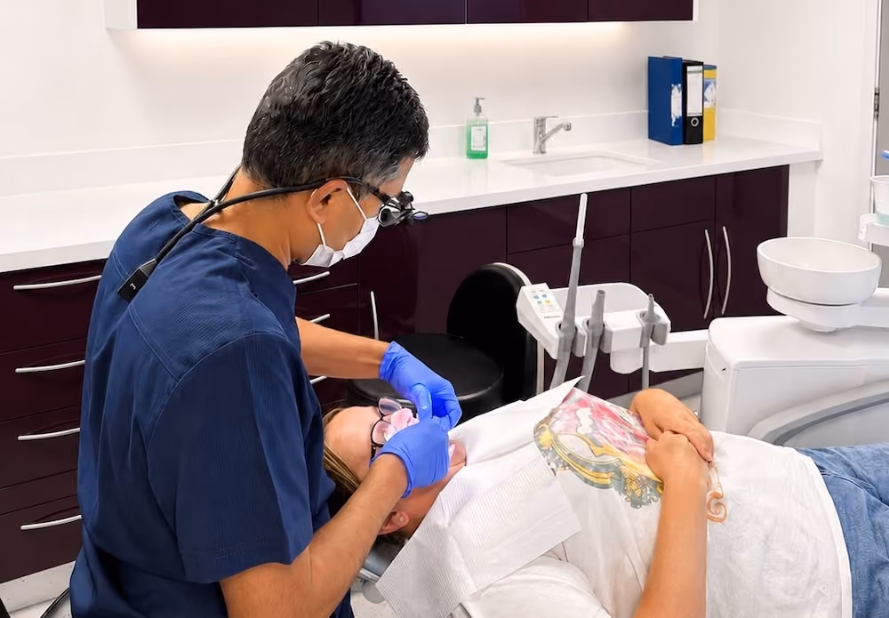 Dentist wearing mask and gloves treating a patient lying in a dental chair in a modern clinic.