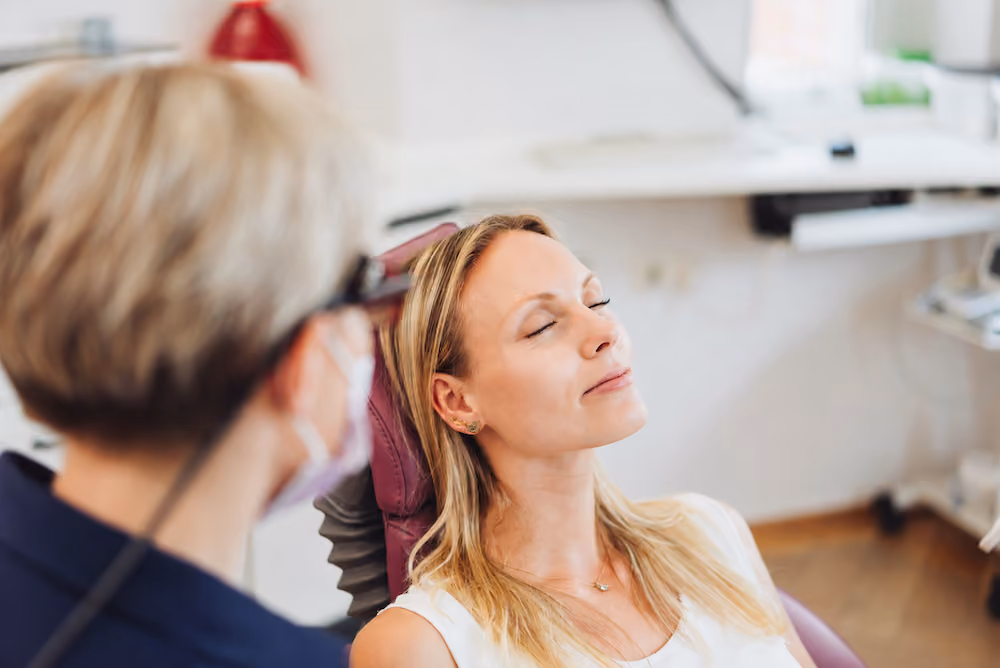 Woman with closed eyes relaxing in a chair as a healthcare professional wearing a mask looks on.