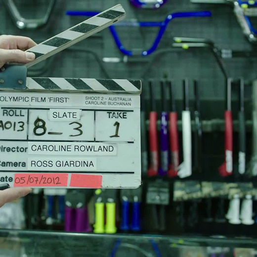 Clapperboard held in front of shelves with colorful bicycle handlebars and grips in a workshop.