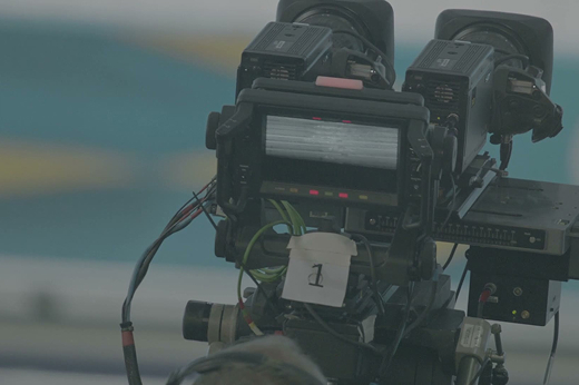 Close-up of a professional video camera with two viewfinders and a label marked '1' attached to it.