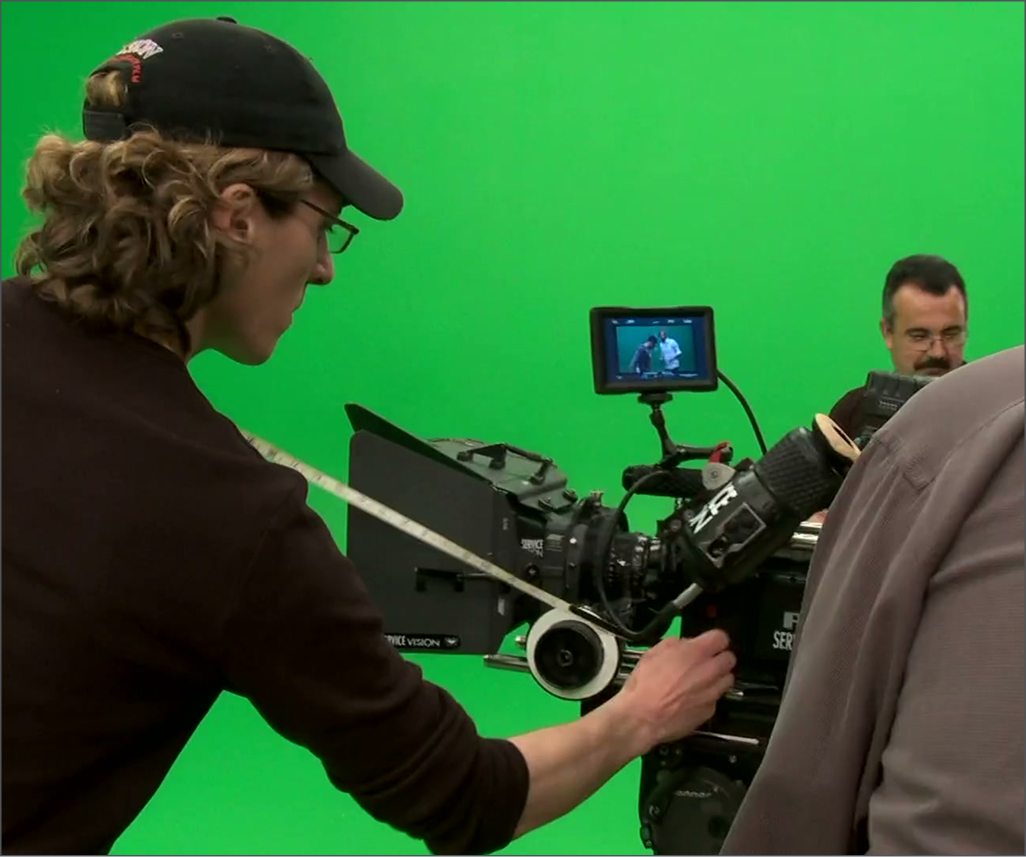 Person operating a professional film camera in front of a green screen.