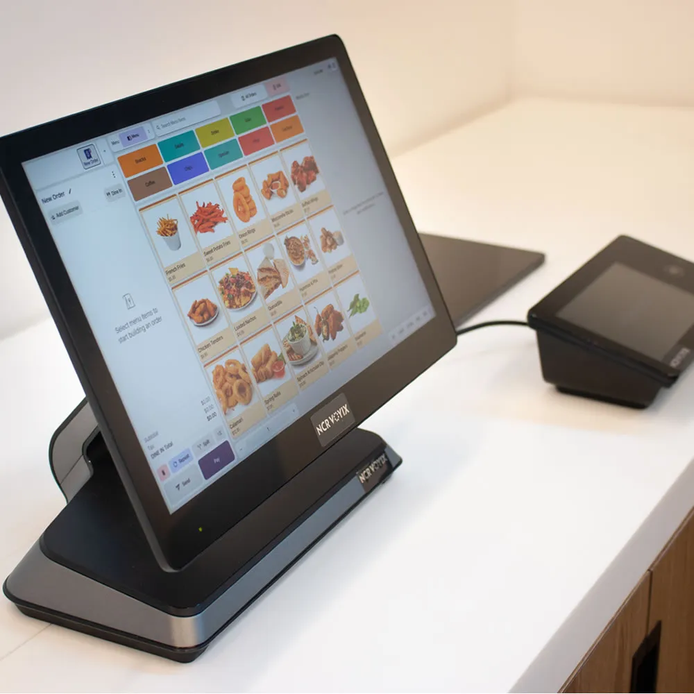 Touchscreen point-of-sale system showing food menu options on a white counter with card reader.
