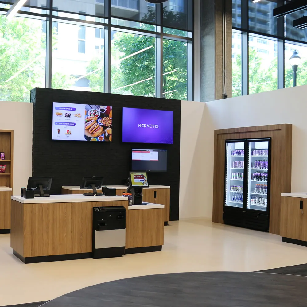 Modern store counter with digital menu boards, wood cabinets, and refrigerated drinks display.