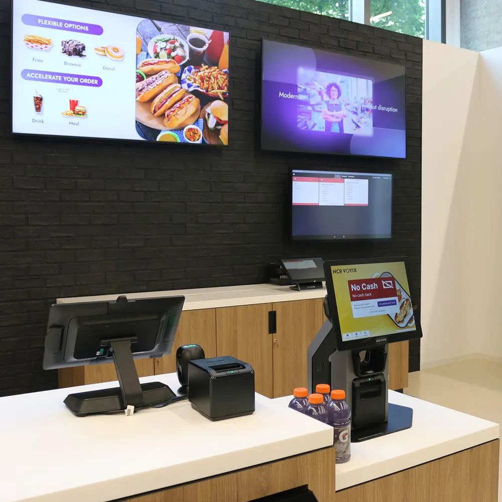 Modern self-checkout counter with touchscreen, barcode scanner, receipt printer, and bottled drinks.