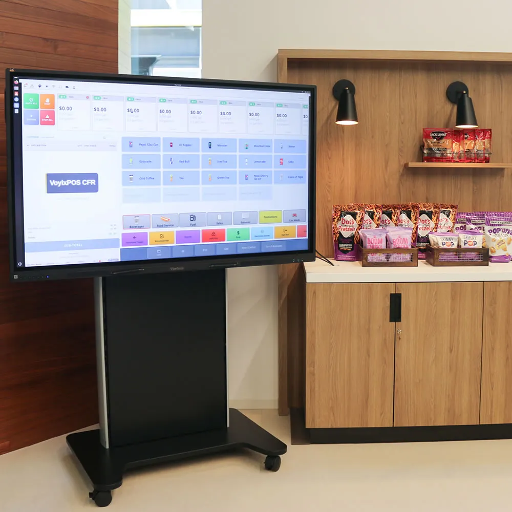 Large screen showing VoyixPOS CFR point-of-sale software next to wooden shelves with snacks and lights.