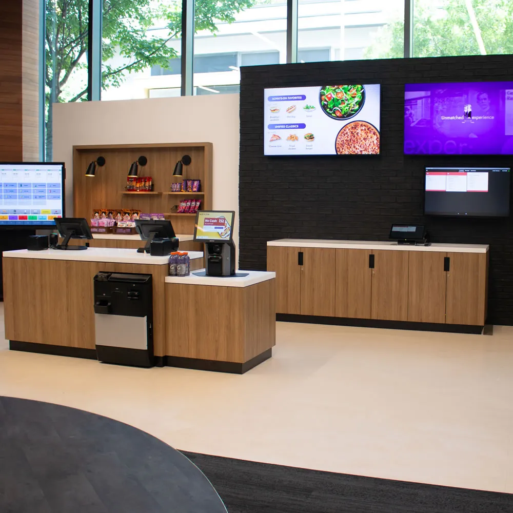 Modern self-service checkout counter with screens, snacks, drinks, and menu displays in a bright store.
