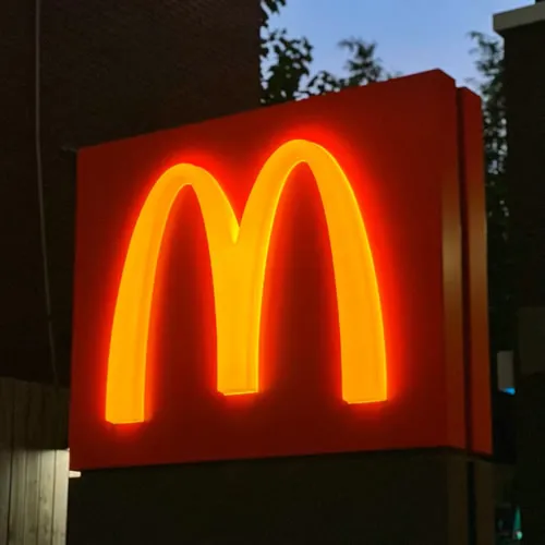 Illuminated yellow McDonald's golden arches sign against a red background at dusk.