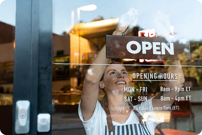 female employee hanging up and open sign in the window of her business