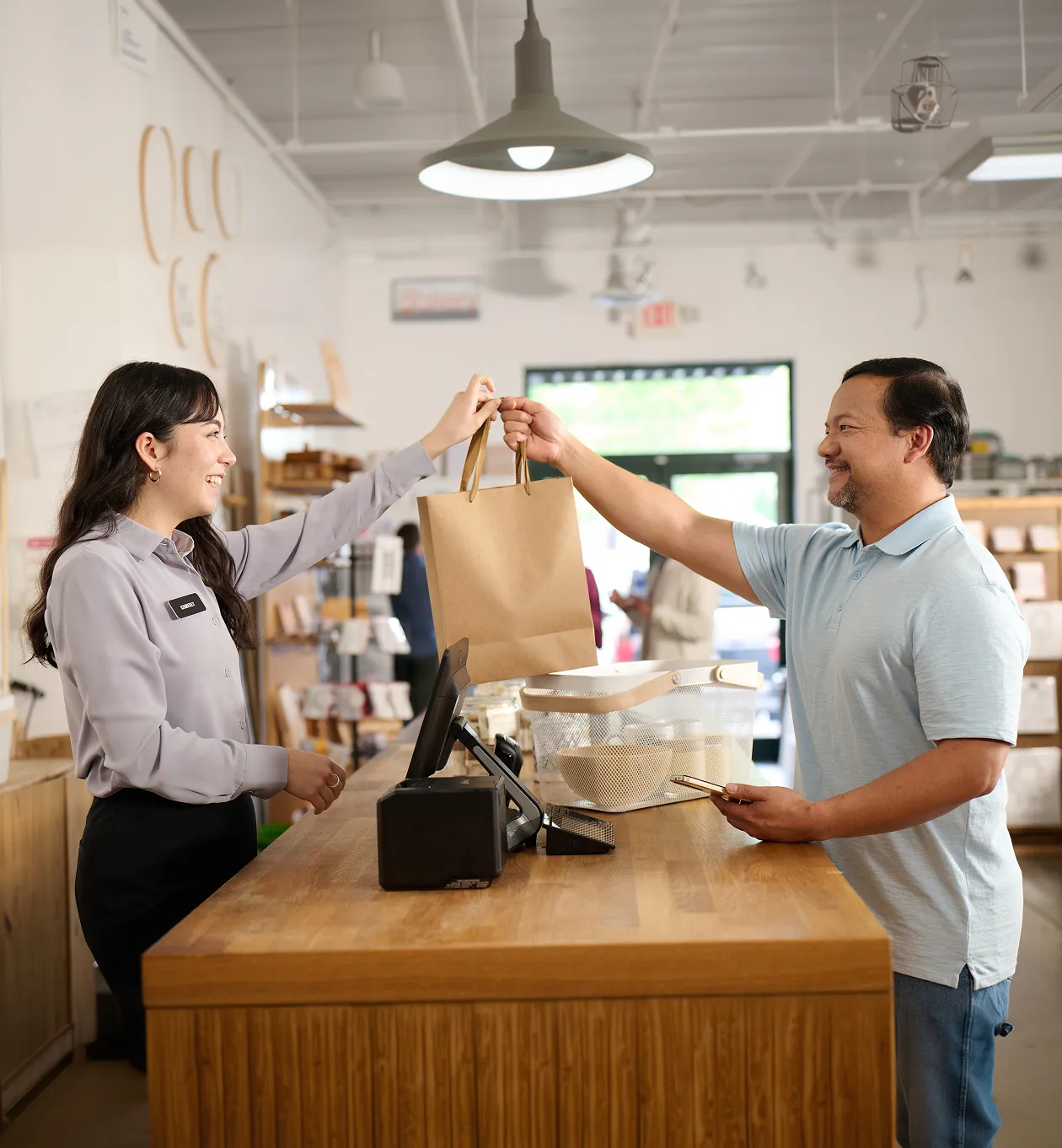 female retail employee handing a male customer his purchase in a brown paper bag