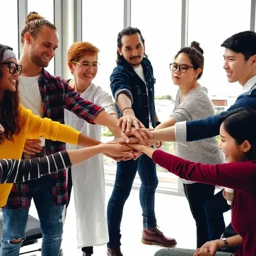 Group of diverse young adults standing in a circle with hands stacked in the center.