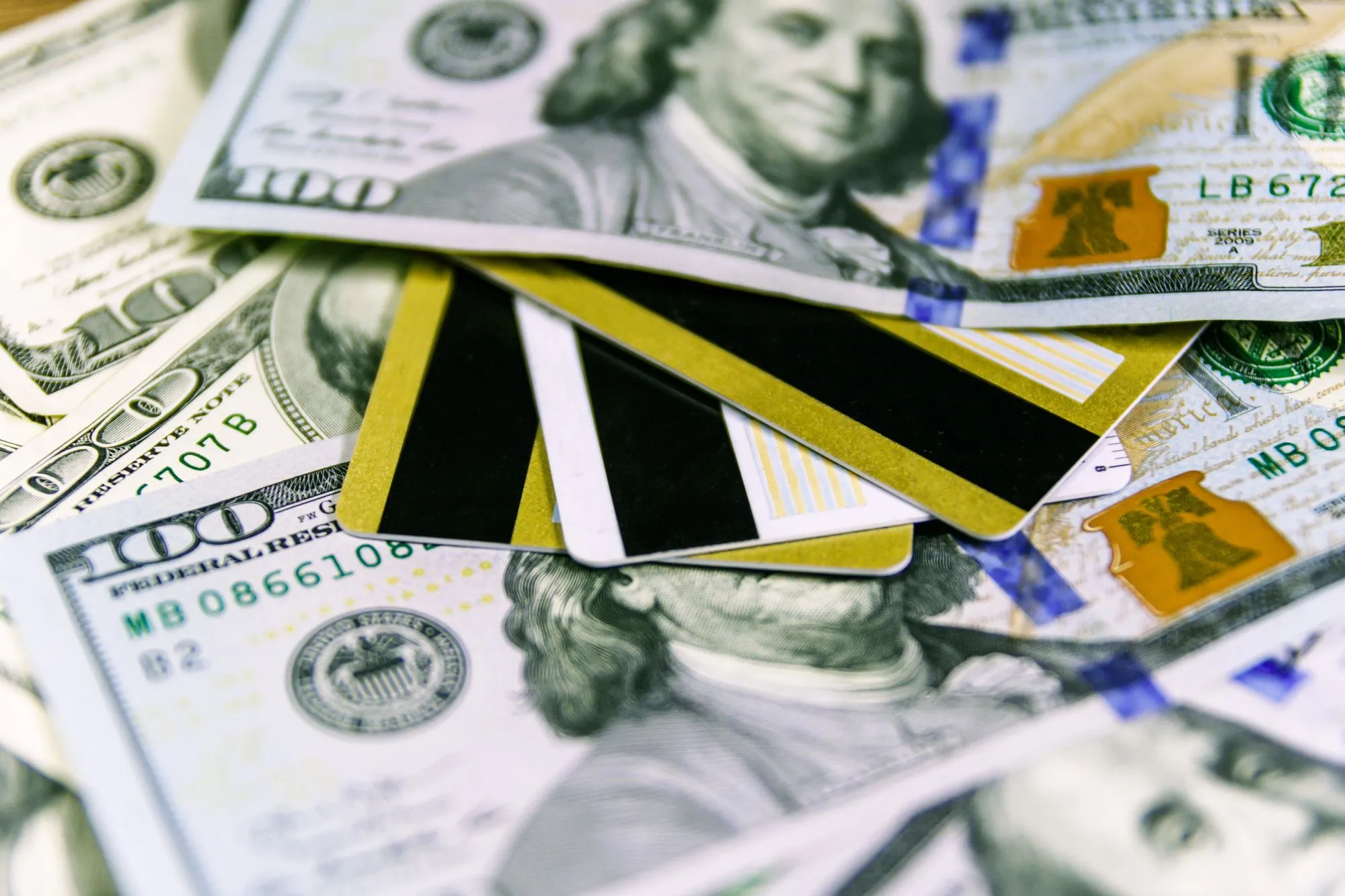 Several credit cards with gold and black stripes lying on US hundred-dollar bills.