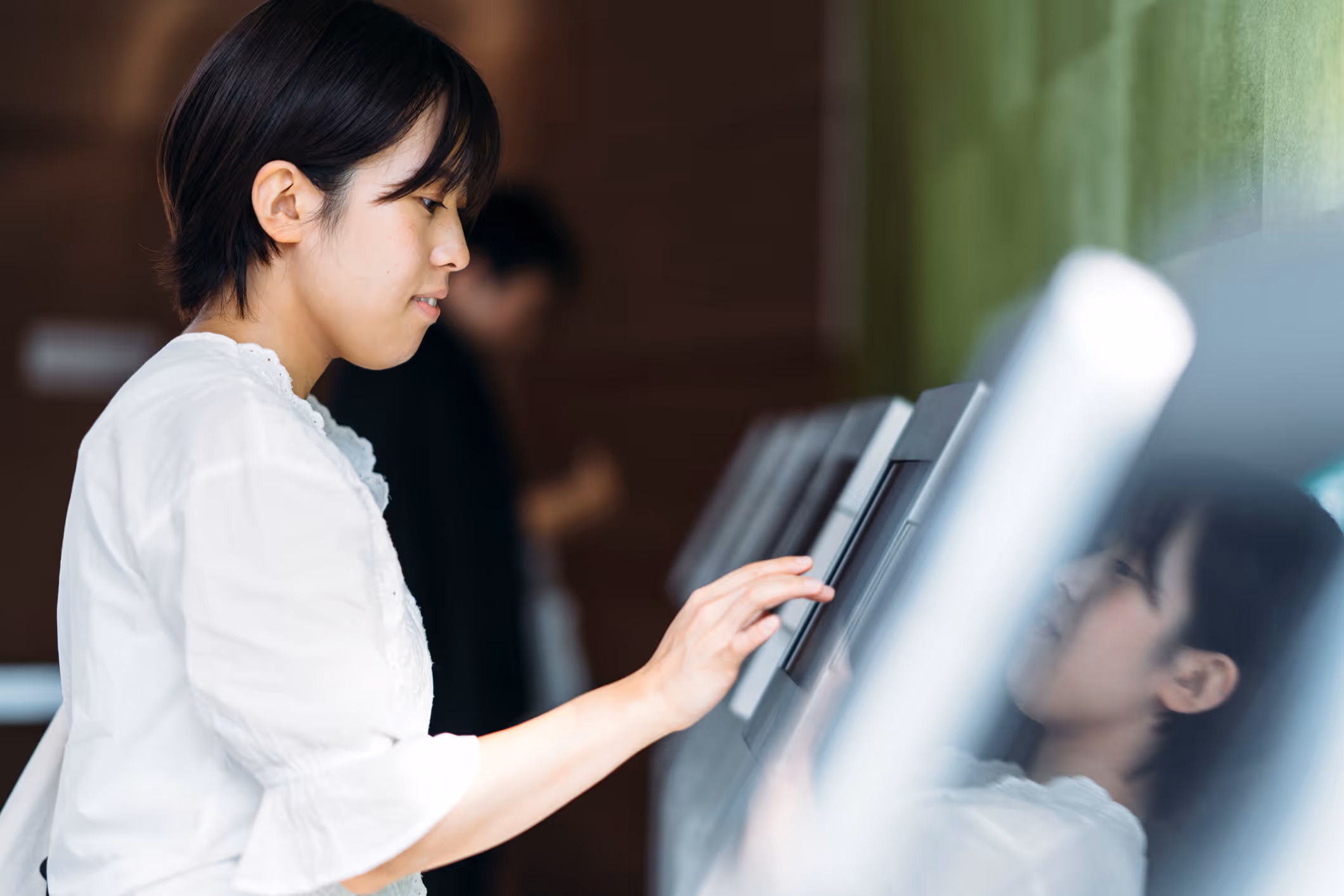 Woman in white blouse using a touchscreen kiosk with her finger in a public setting.