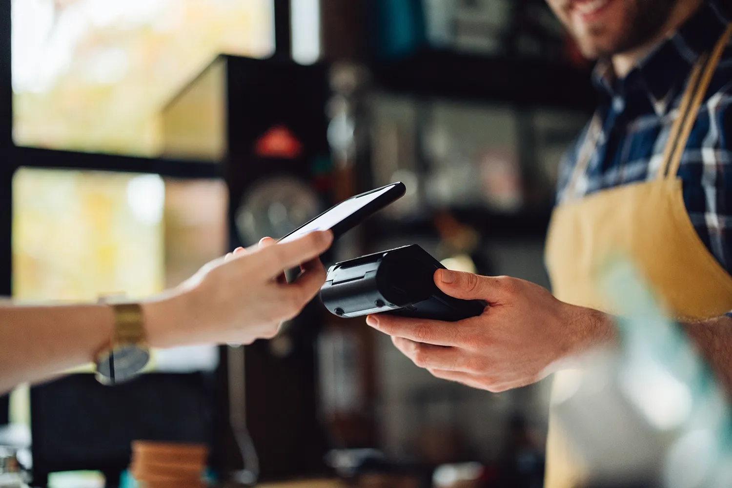 Person holding payment terminal while customer pays with mobile phone in a store.