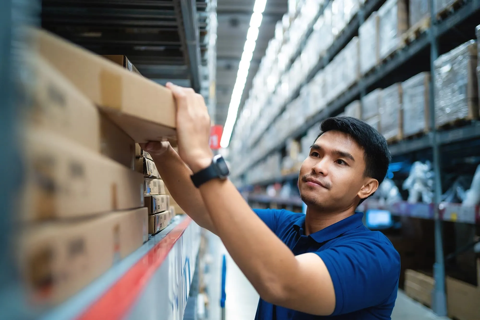 Worker in blue shirt placing a cardboard box on a warehouse shelf.