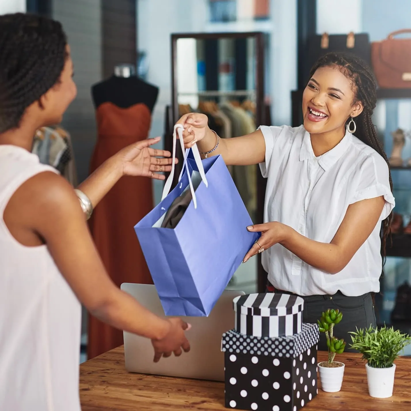 Smiling shop assistant handing a blue shopping bag to a customer inside a clothing store.