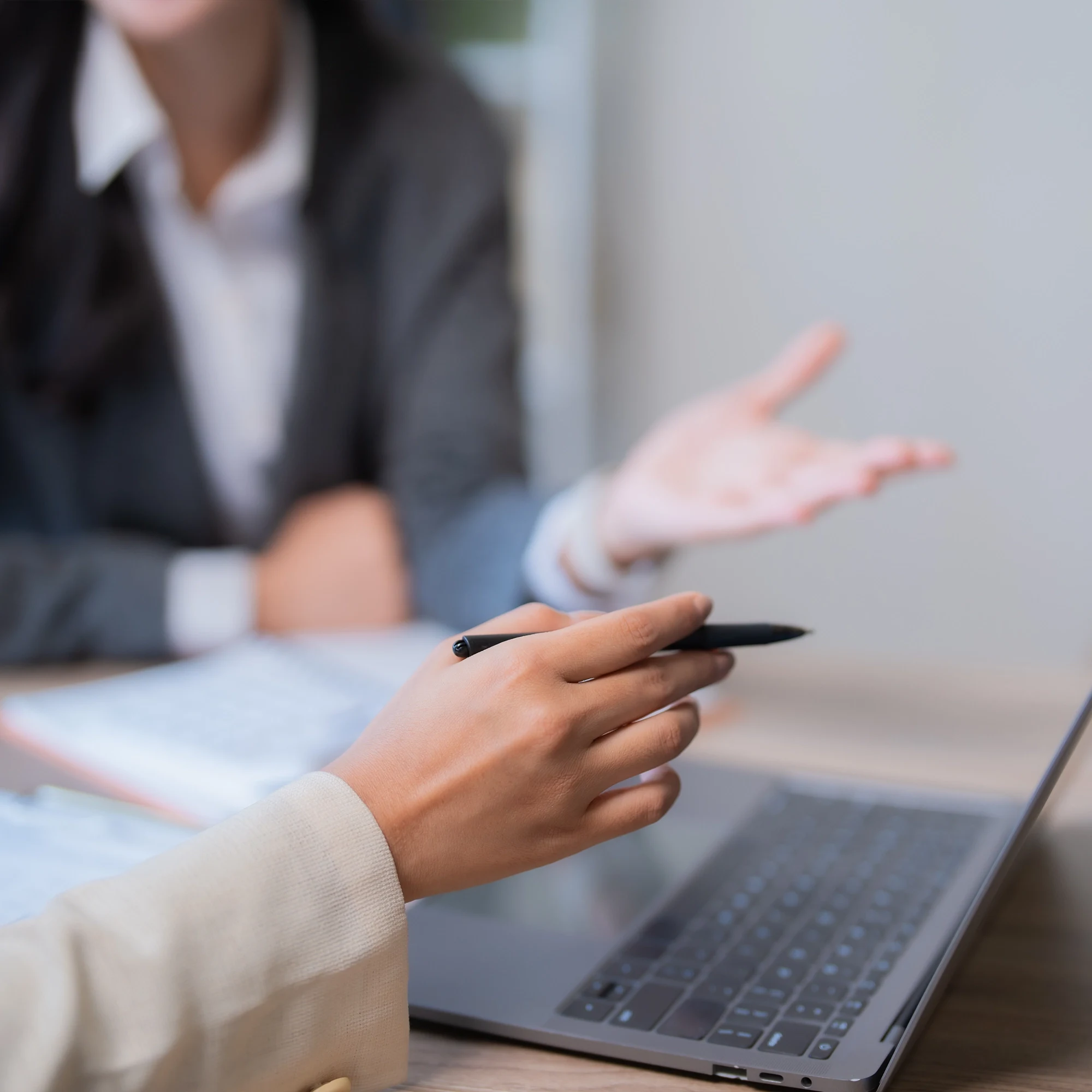 Two businesspeople having a discussion over a laptop, one holding a pen and gesturing.