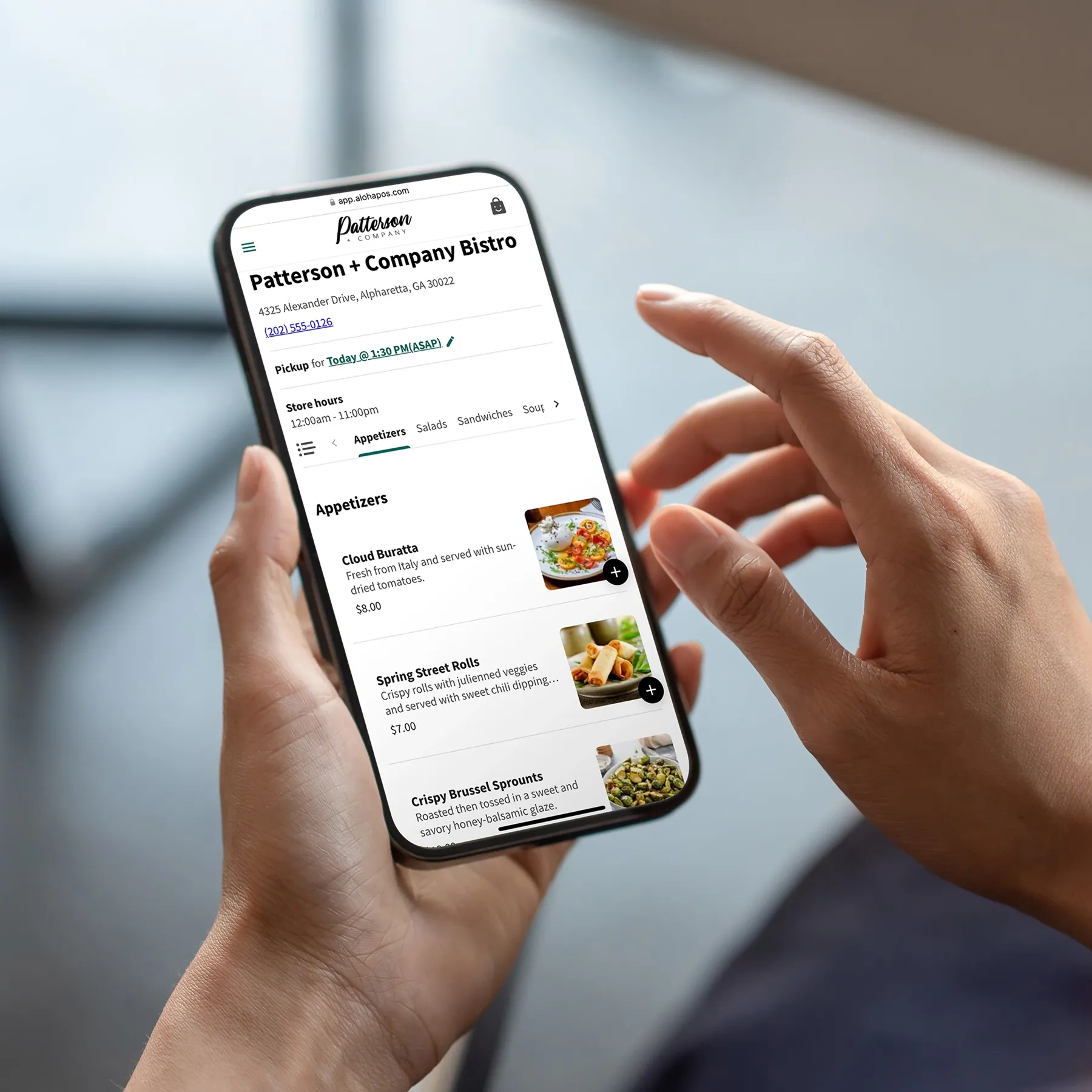 Person holding iPhone showing Patterson + Company Bistro menu app with appetizers listed.