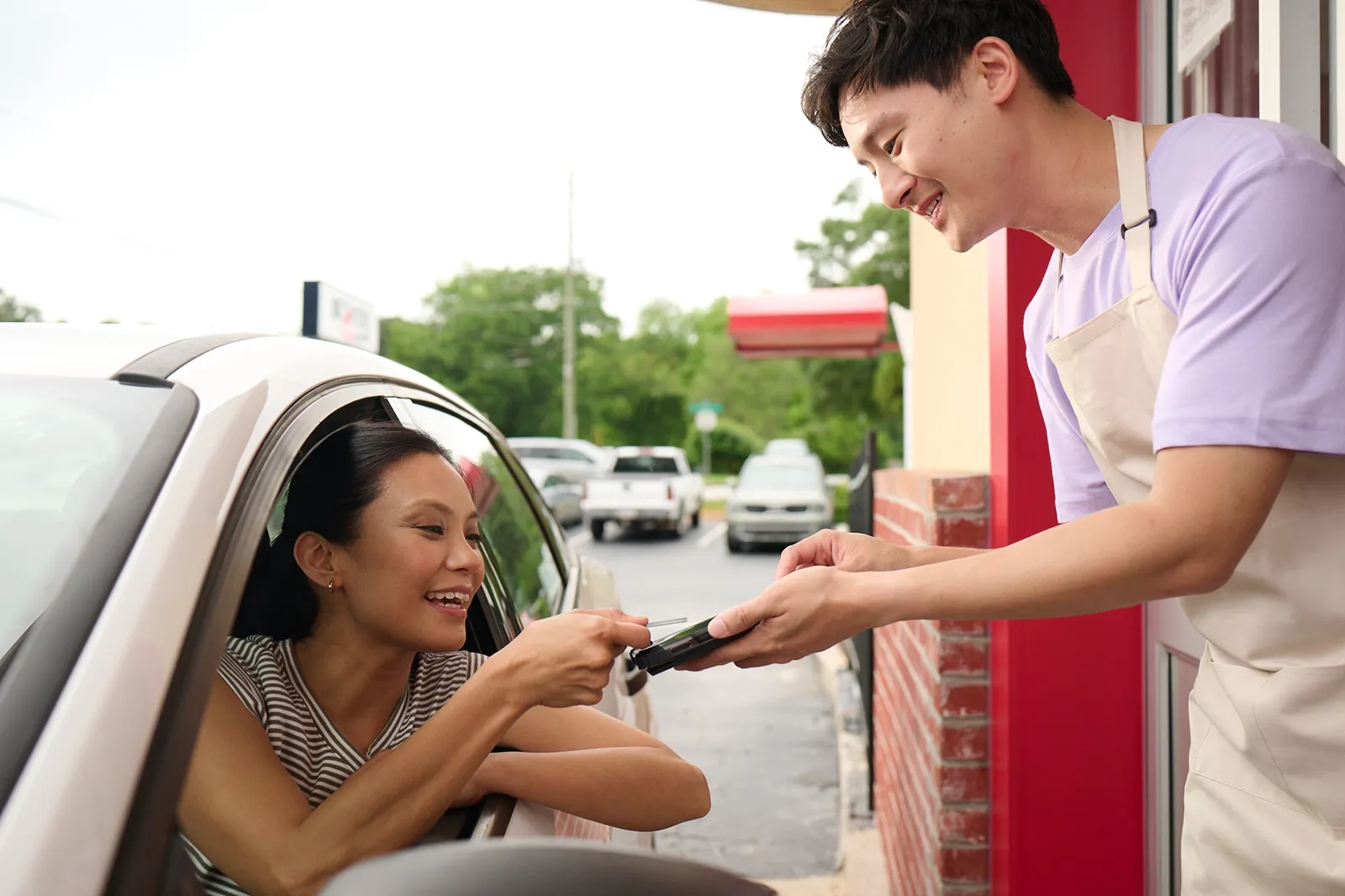 Woman in car paying a smiling drive-thru worker with a card reader device.