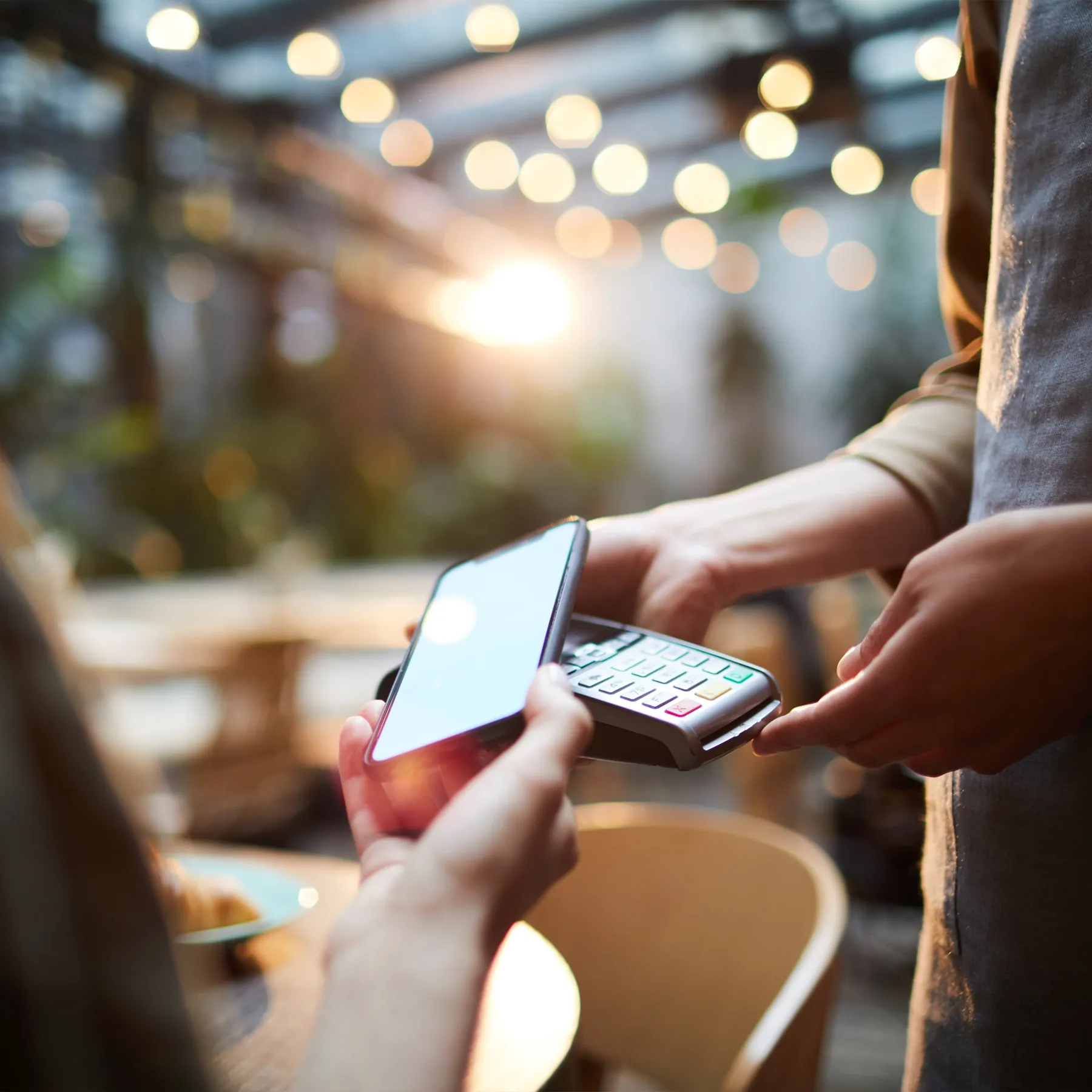 Person making a contactless payment with a smartphone on a card reader in a cafe.