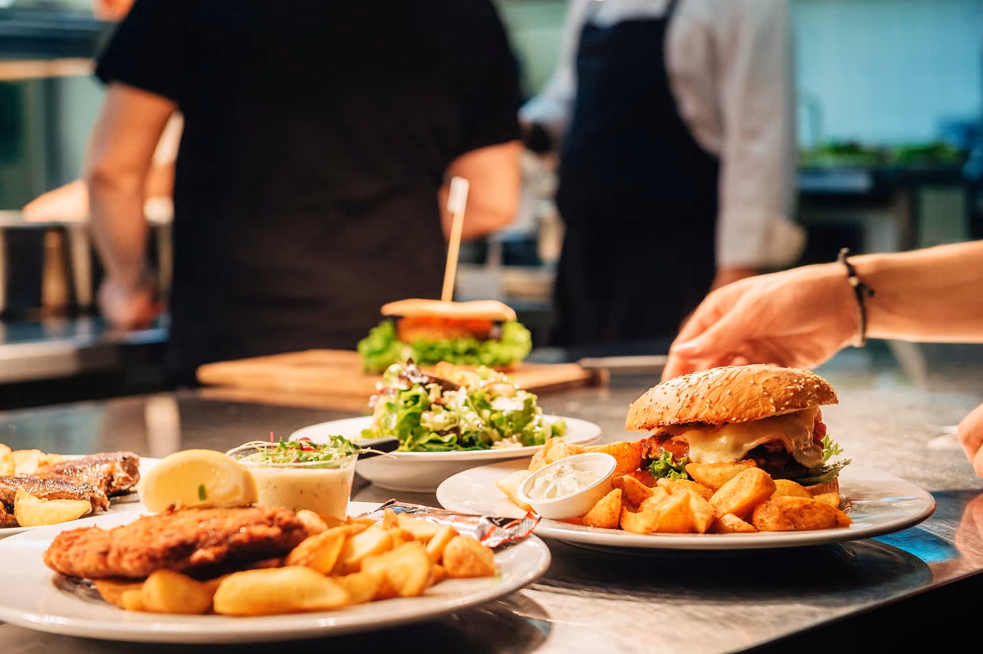 Plates with burger, salad, fried chicken, and potato wedges served on a restaurant counter.