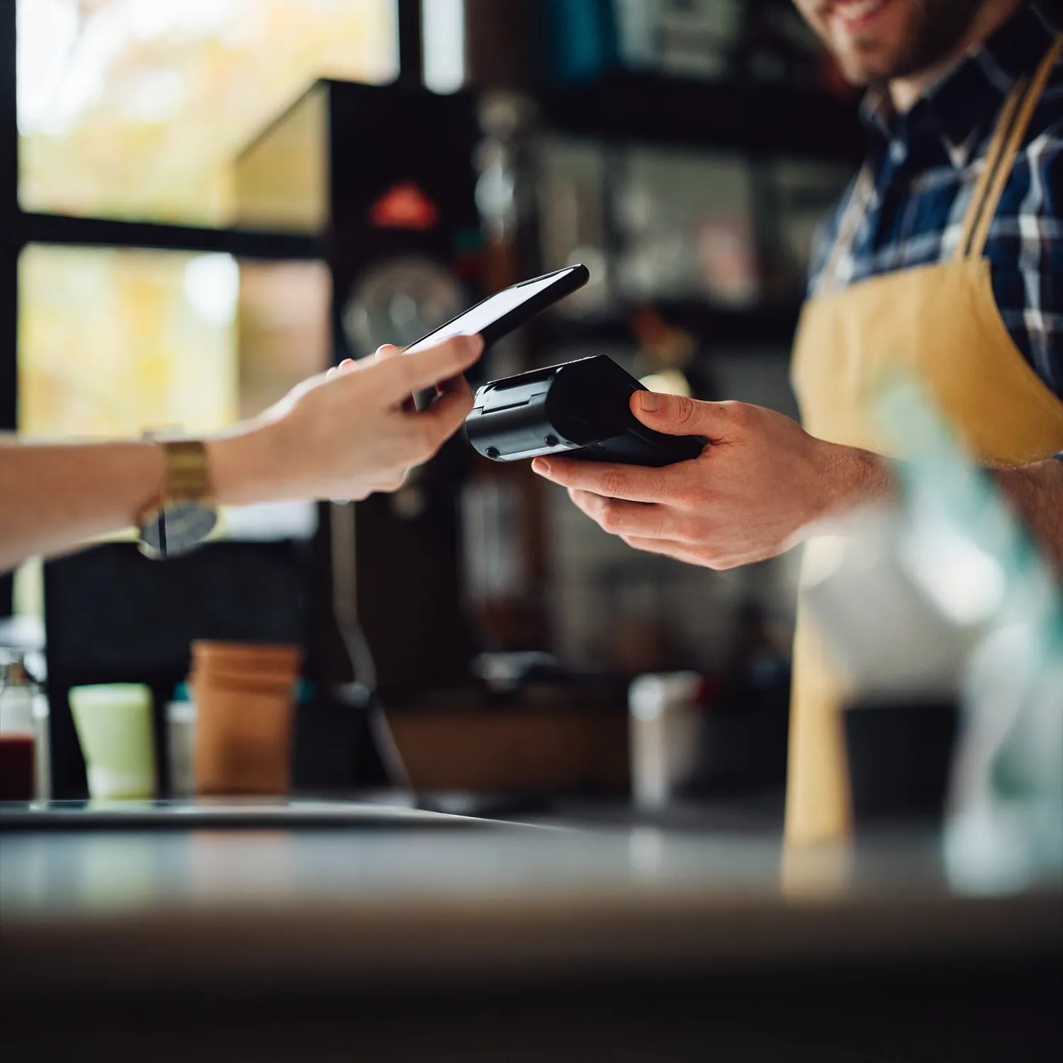 Customer makes a contactless mobile payment using a smartphone at a cafe counter.