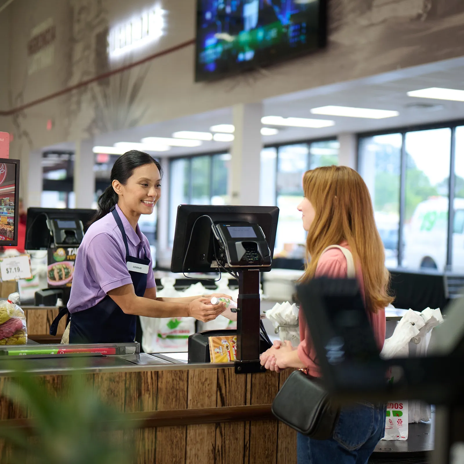 Grocery store cashier handing a product to a customer at the checkout counter.