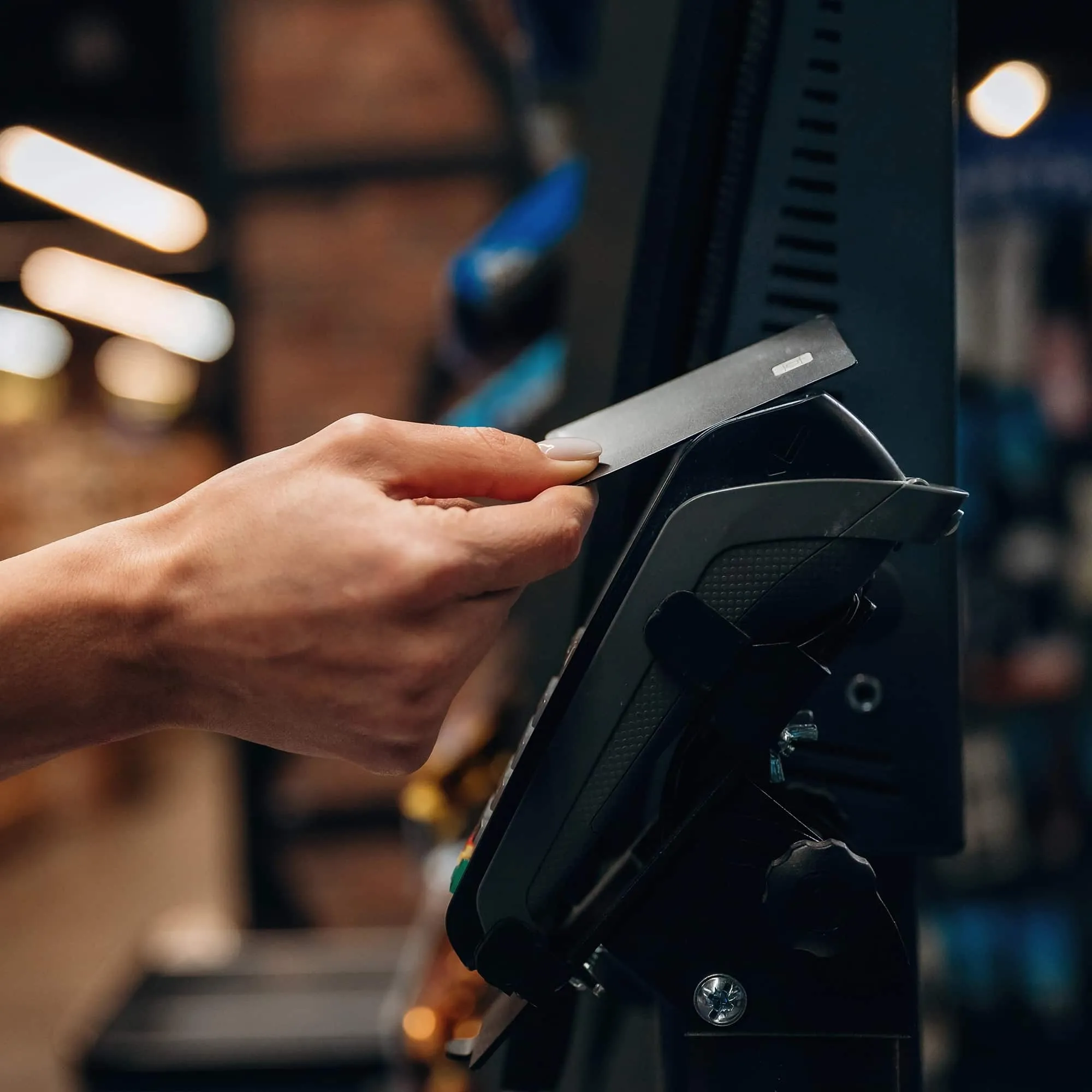 Hand holding a credit card near a payment terminal for a contactless transaction.