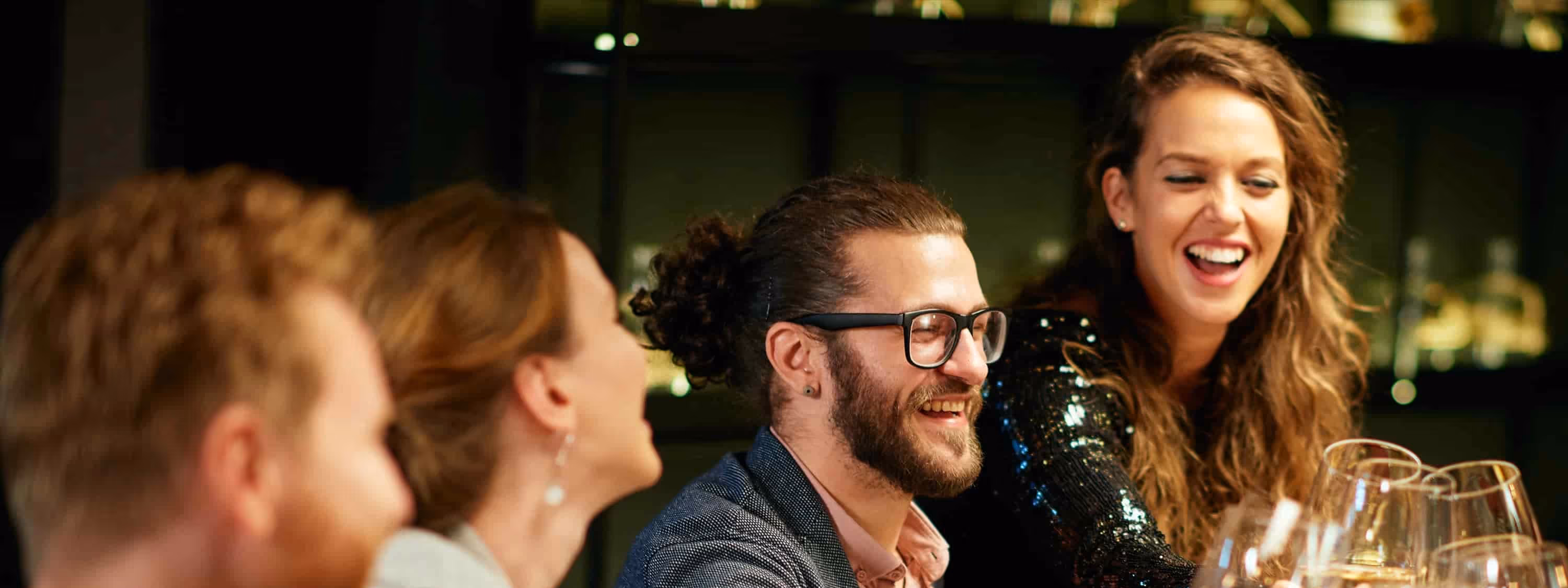 Group of four friends laughing and clinking wine glasses during a night out.