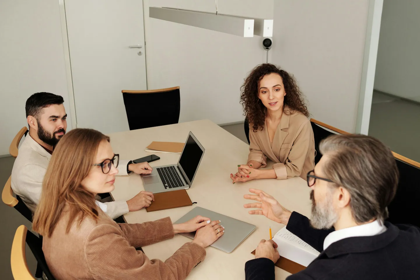 Four professionals having a discussion around a conference table with laptops and notebooks in a modern office.