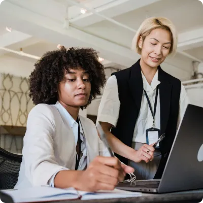 Two professional women collaborating at a desk with a laptop and documents in an office.
