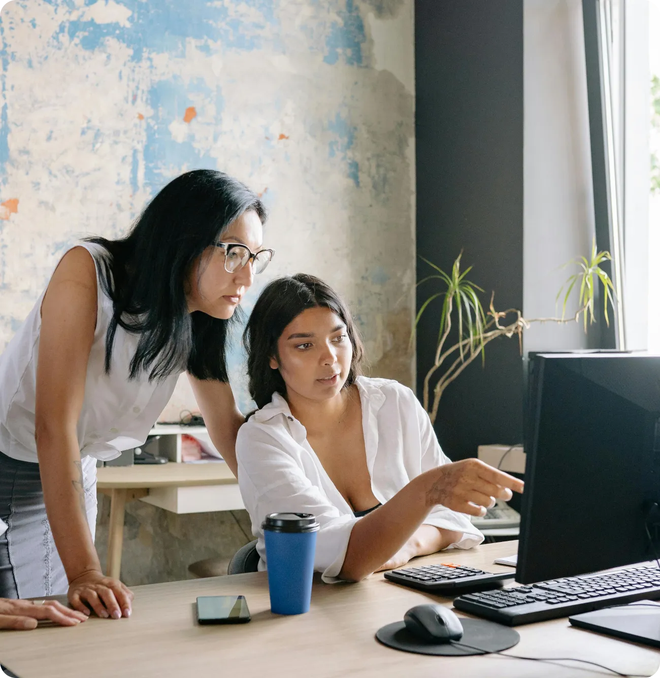 Two women looking at a computer monitor, one sitting and pointing at the screen and the other standing beside her.