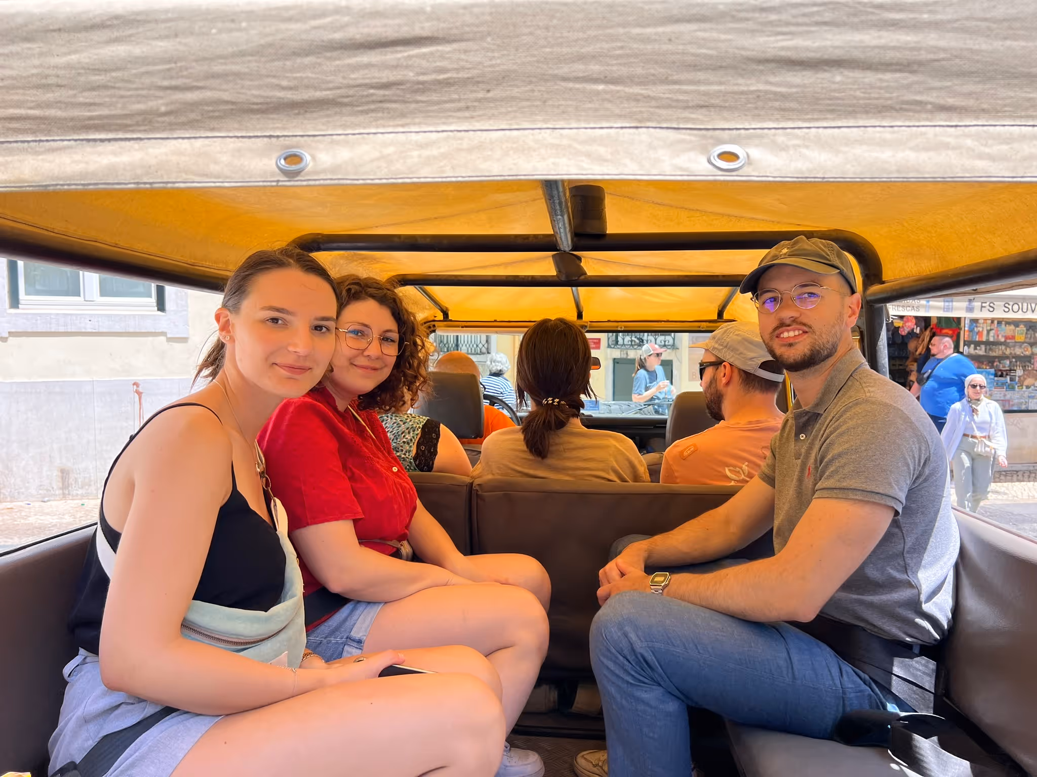 Quatre jeunes adultes souriants assis à l'intérieur d'un véhicule découvert avec une toile jaune.