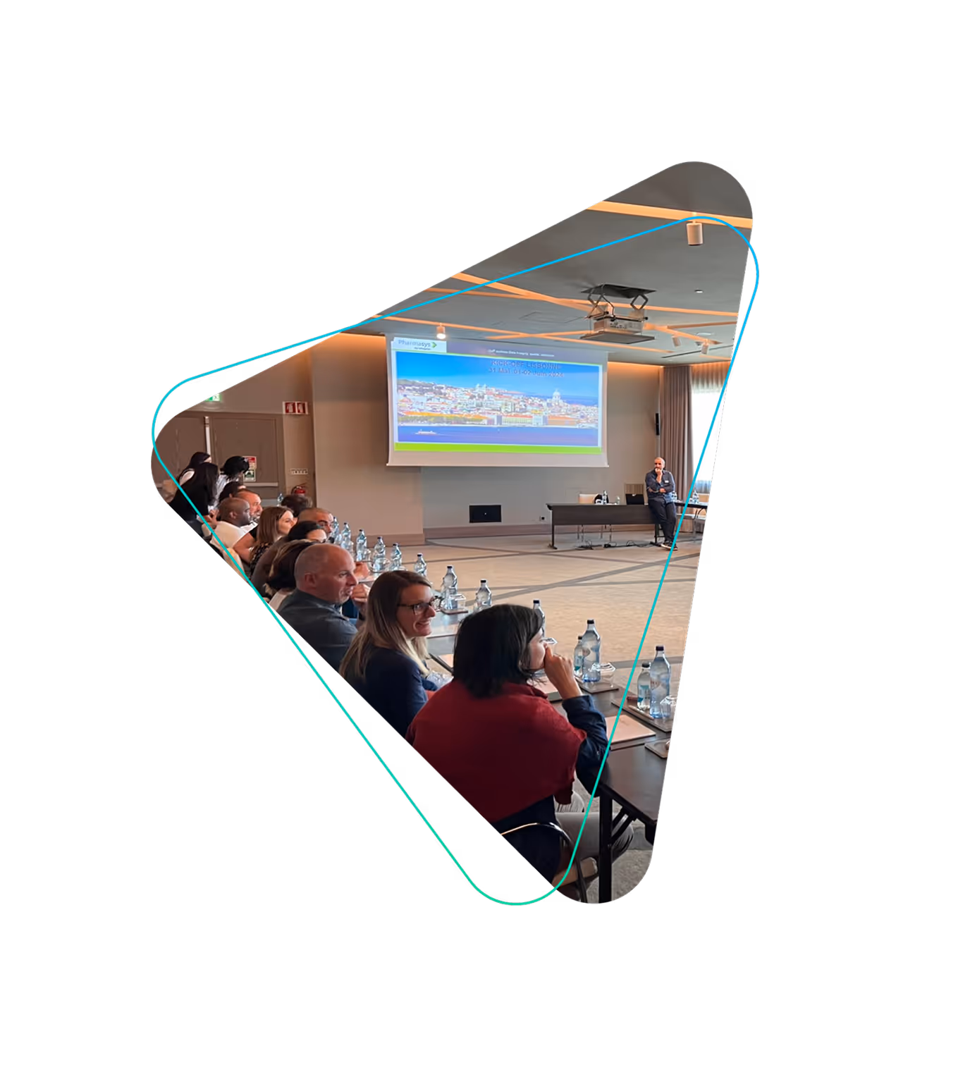 Réunion en salle avec plusieurs personnes assises à une table, un homme debout devant un écran de projection affichant une image de Lisbonne.