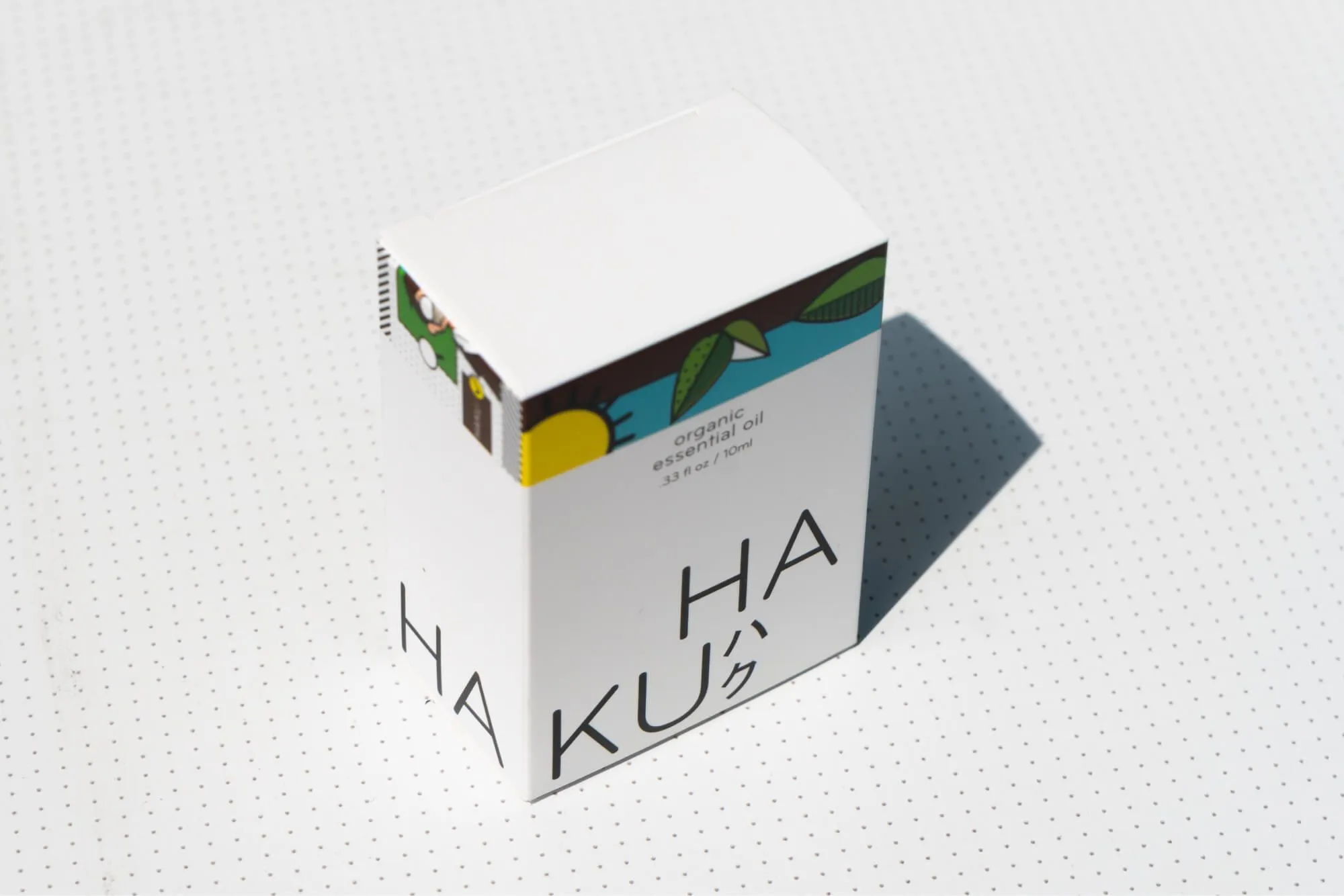 White box of HAKU organic essential oil with colorful leaf and sun illustrations on top edge.