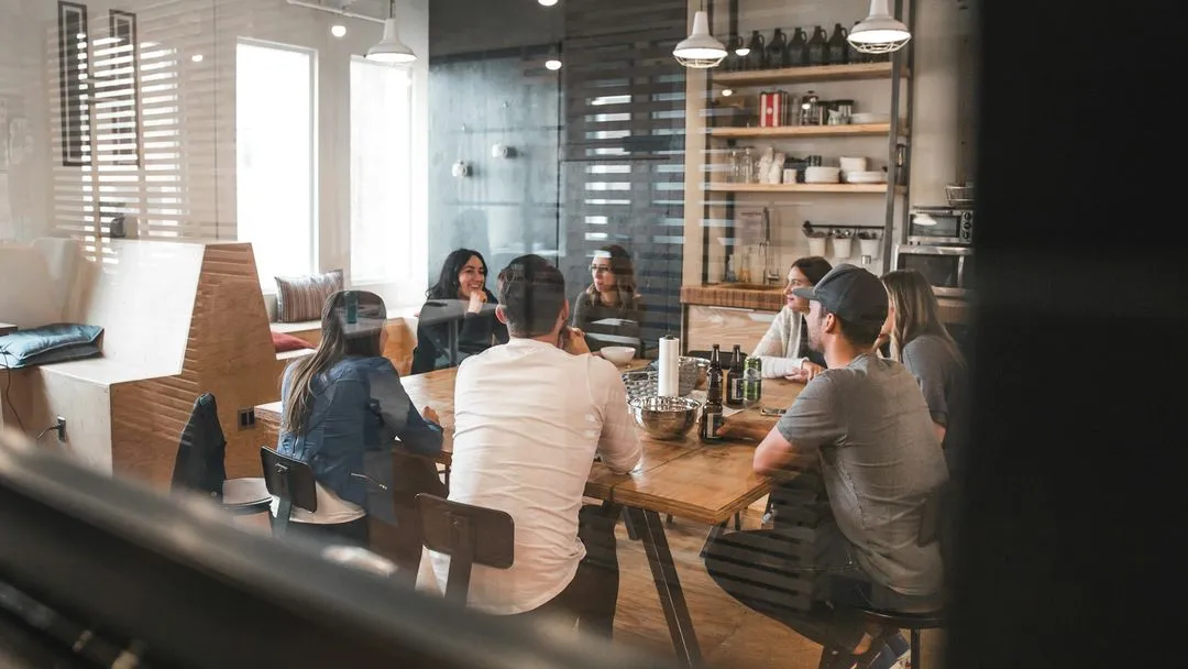 Group of people sitting around a wooden table in a modern kitchen having a discussion.