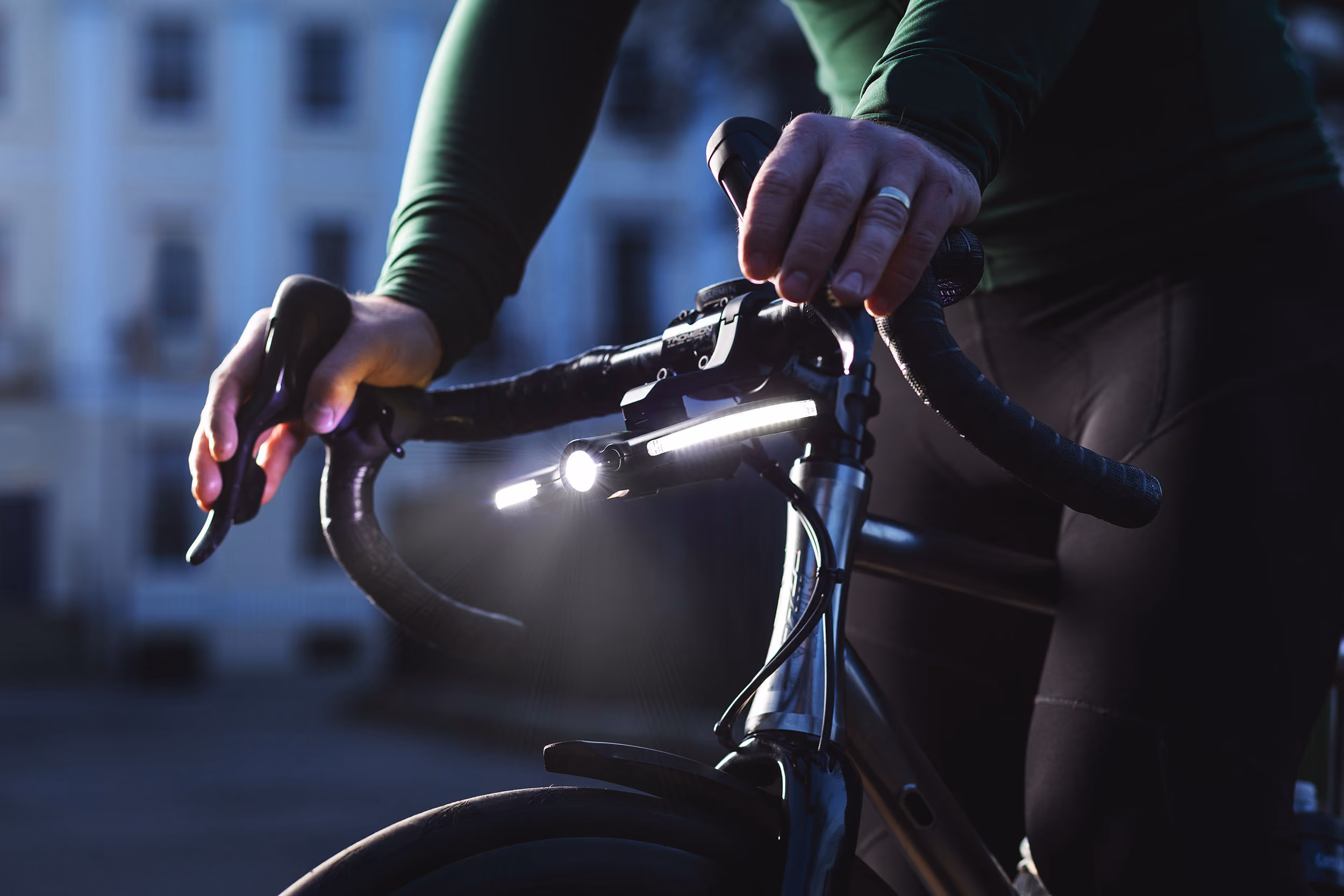 Close-up of a cyclist's hands on handlebars with bike lights on in low light.