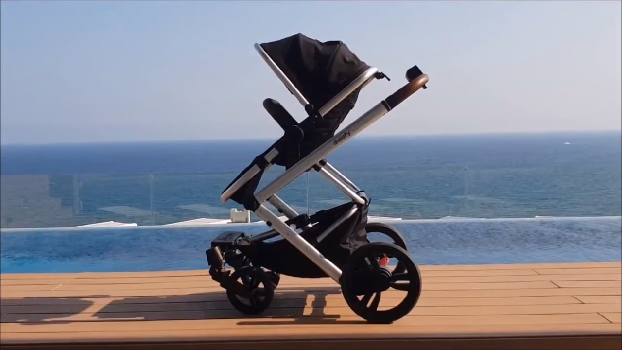 Modern baby stroller with black seat on wood deck overlooking blue ocean and clear sky.