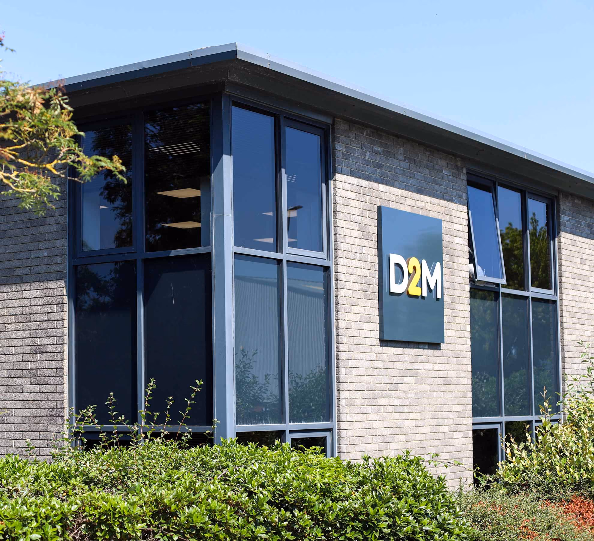 Exterior of a modern brick office building with large windows and a D2M sign mounted on the wall.