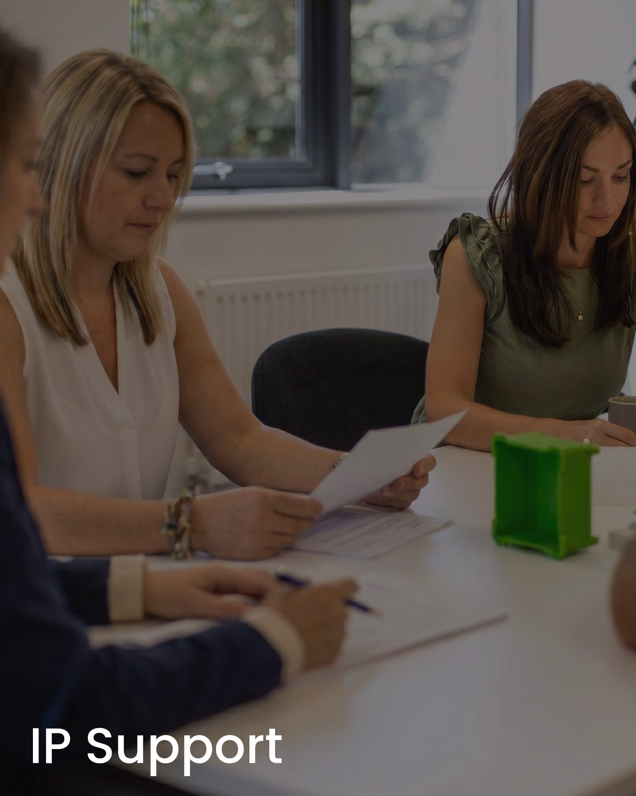 Three people sitting at a table reviewing documents in a meeting room with a window in the background.
