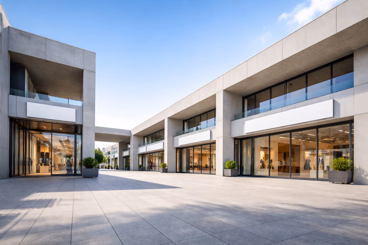 Modern outdoor shopping center with large glass windows and empty storefronts under a clear blue sky.