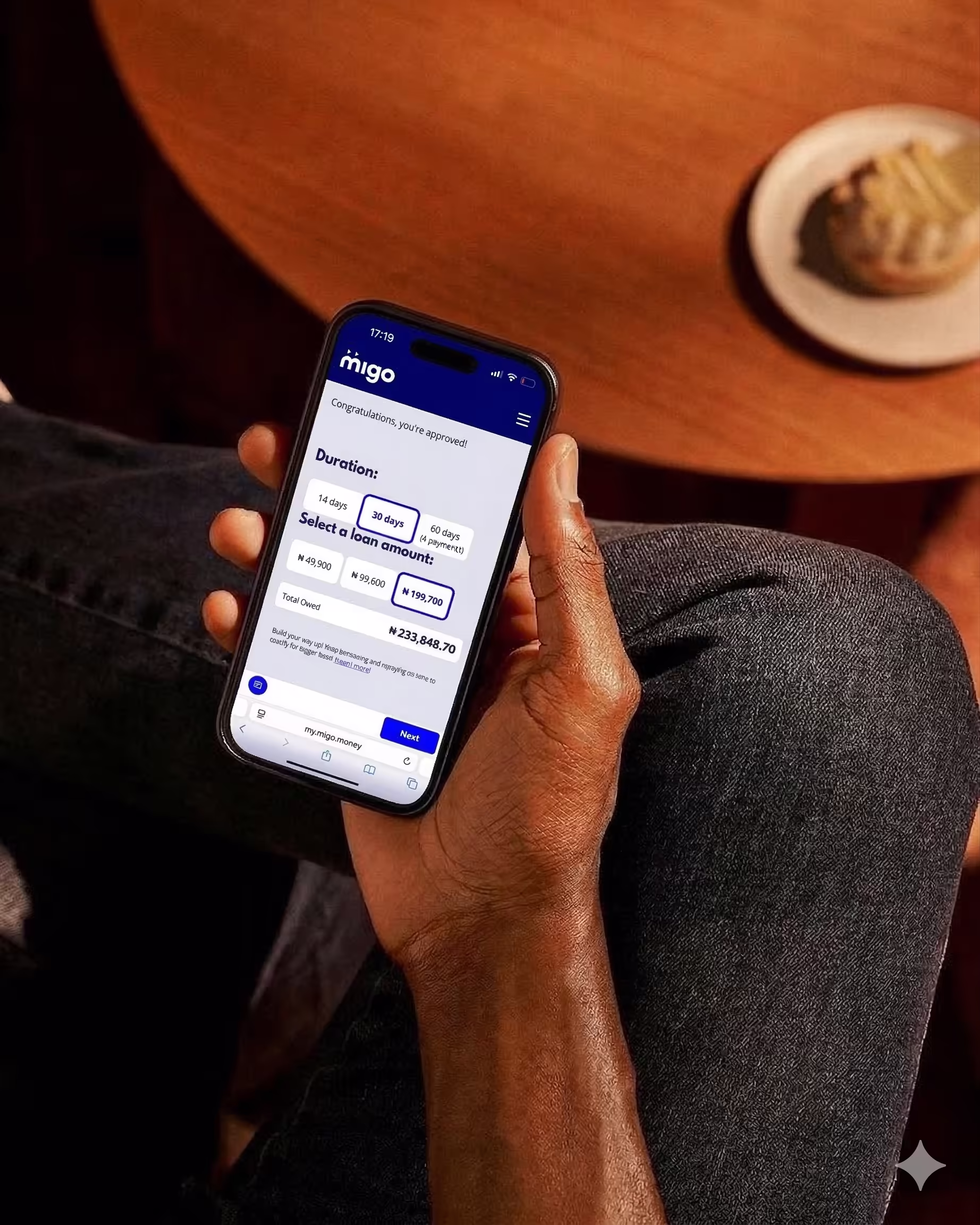 Hand holding smartphone displaying Migo loan approval screen with options for loan duration and amount.